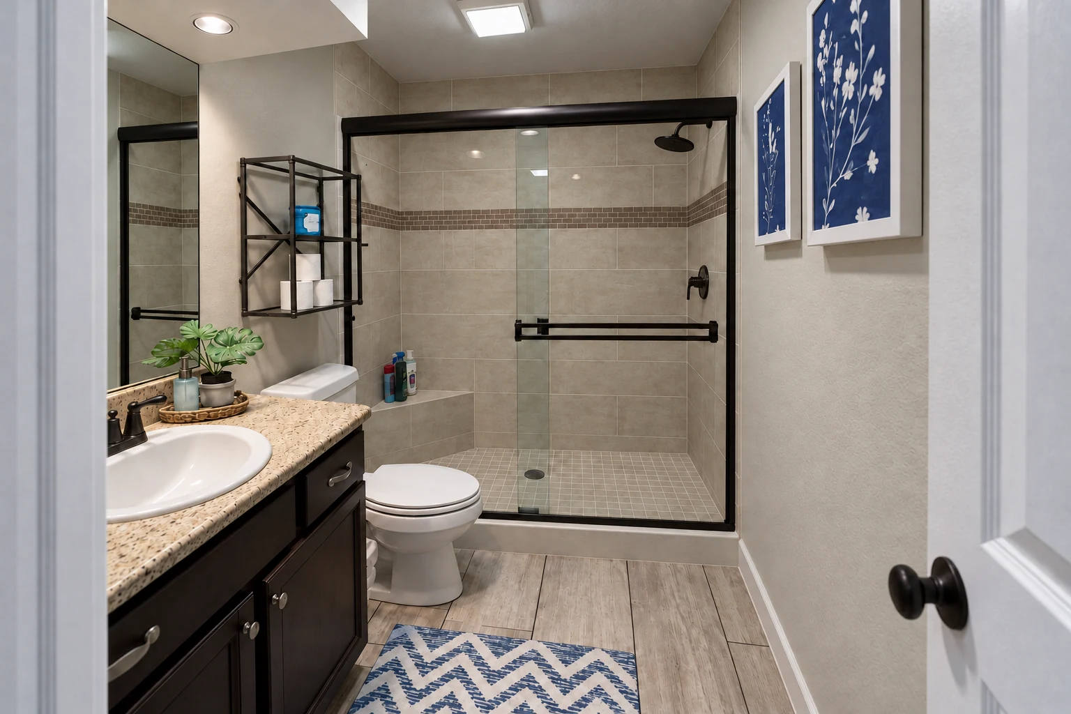 Completed McKinney walk-in shower with full-height light tile, taupe accent stripe, bronze-toned fixtures and an updated dark vanity